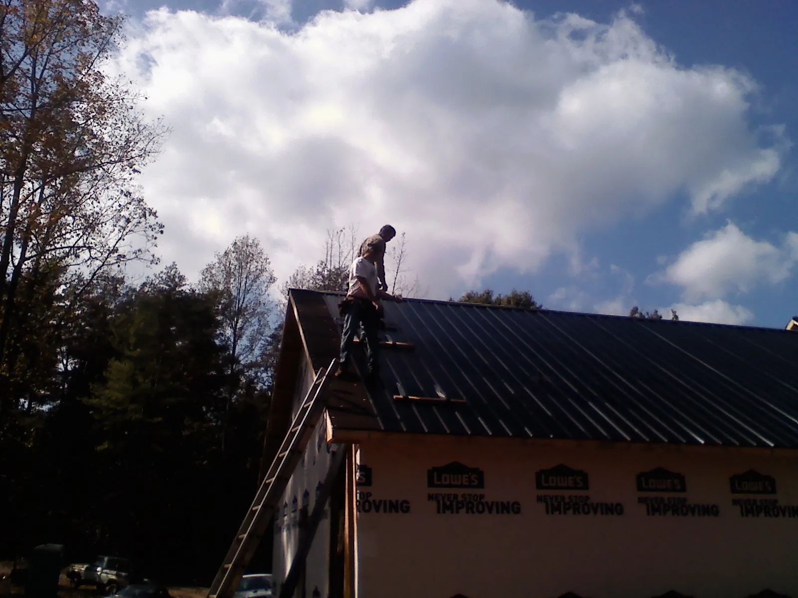Roofer fastening dark metal panels high against a cloudy sky, from a Roof Inspection job in Willow Grove