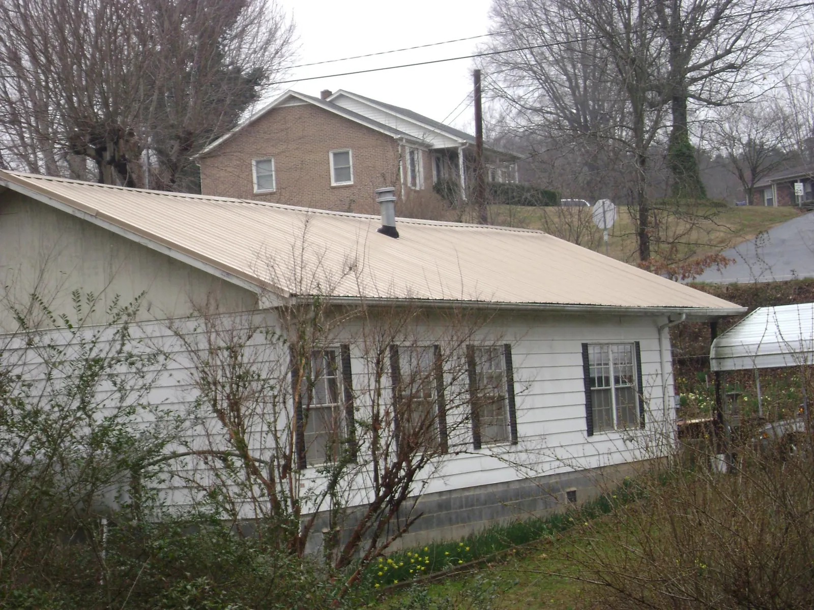 Tan metal roof on a white sided house set into a hillside — Commercial Roofing by Roofing Brothers in Willow Grove